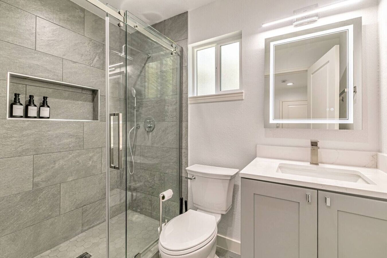A modern bathroom with a glass-enclosed shower, a toilet, and a vanity with a mirror.