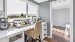 A modern kitchen with a large window, a coffee maker, tea and coffee containers, and a wicker chair. - 4BR3.5BA w/Epic SJ Valley Views! (San Jose)