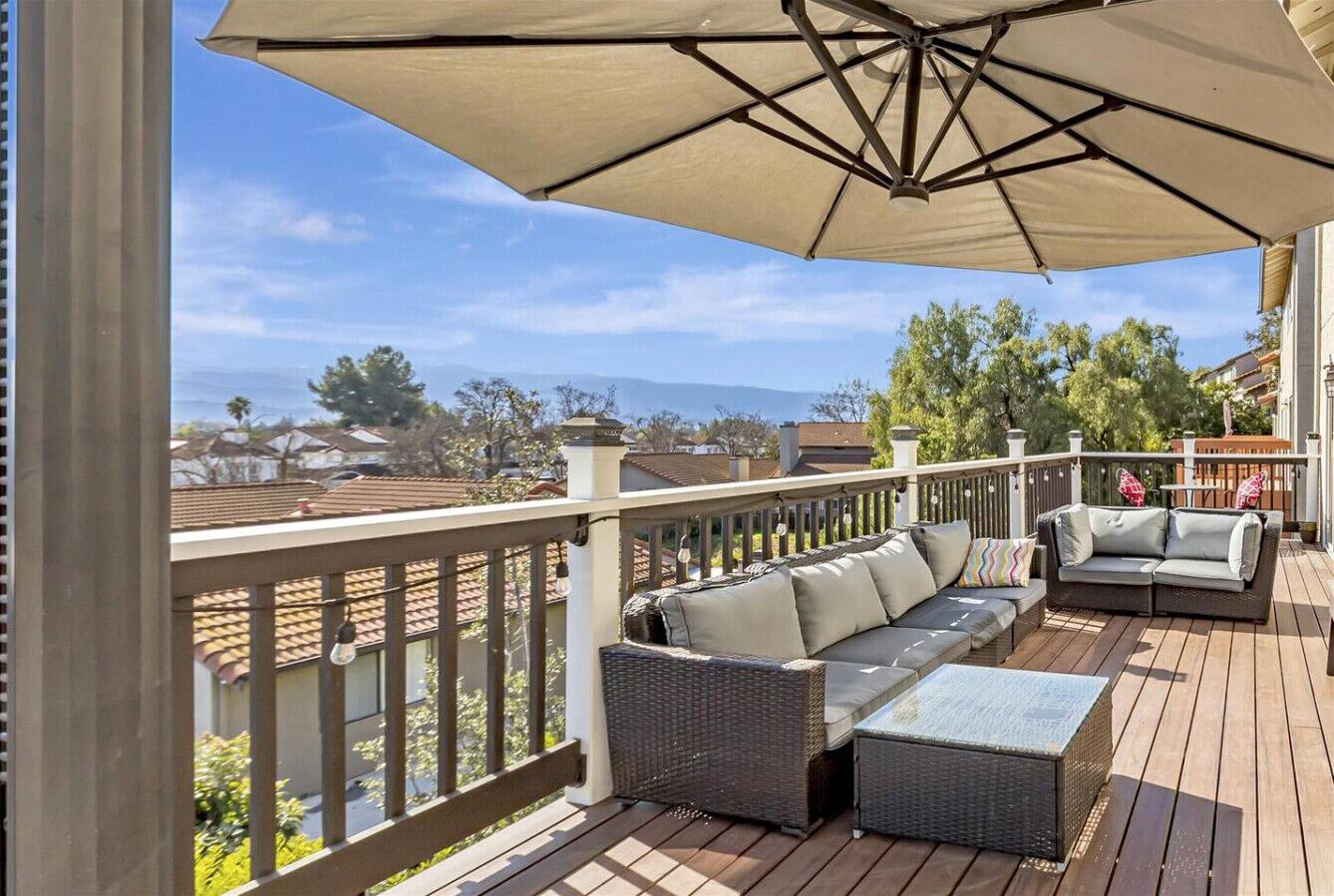 A covered outdoor deck with a sofa and a table, overlooking a residential area.