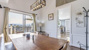 A spacious dining area with a large wooden table, a chandelier, and a view of the outdoors through a large window. - 4BR3.5BA w/Epic SJ Valley Views! (San Jose)