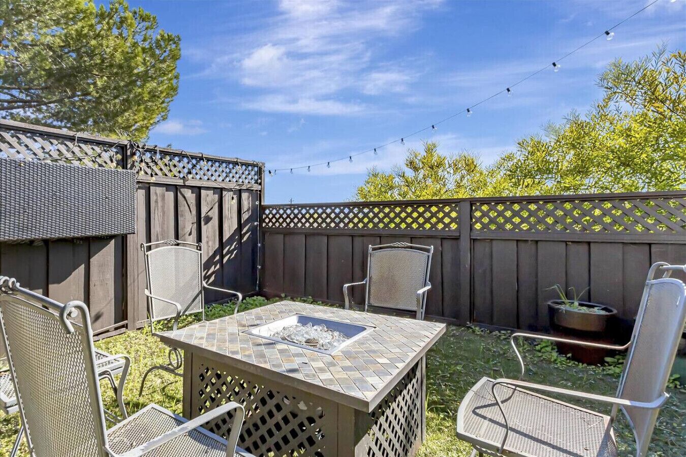 A patio area with a table and four chairs, surrounded by a wooden fence and string lights.