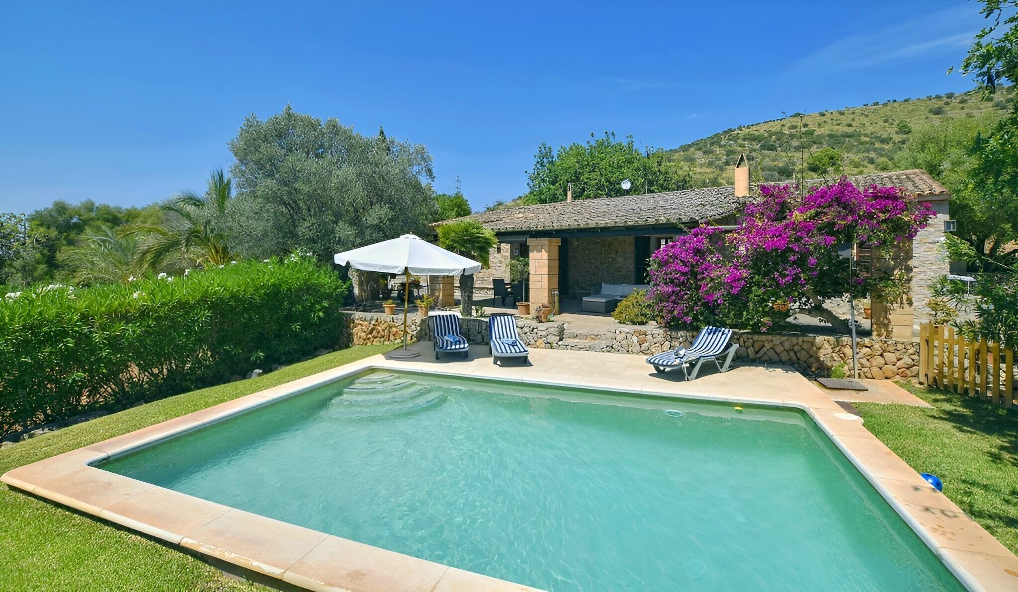 A swimming pool with lounge chairs, a covered seating area, and a stone building with a garden.