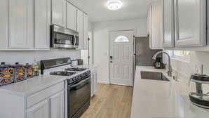 A compact kitchen with white cabinets, a stainless steel stove, a microwave, and a sink. - Downtown 1bd/1ba ADU (Sunnyvale)