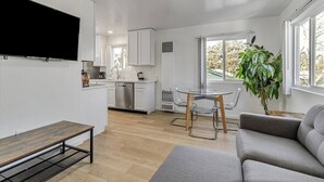 A modern living room with a flat-screen TV, a grey sofa, a wooden coffee table, and a dining area with a glass table and chairs. - Downtown 1bd/1ba ADU (Sunnyvale)