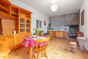 A dining area with a wooden cabinet, a table with a red tablecloth, chairs, a wine bottle, and a stone fireplace.