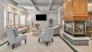 Un salon moderne avec une cheminée, un canapé, deux fauteuils à motifs, une table basse et un téléviseur fixé au mur.