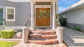 Une maison à deux étages avec un porche à l’avant, une porte d’entrée en bois et un escalier en briques menant à l’entrée.