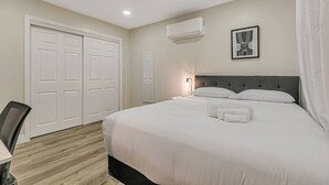 Una camera da letto con un letto grande, una scrivania e una sedia. Si notano due porte e un condizionatore d'aria a parete.