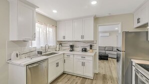 Una cucina moderna con mobili bianchi, lavastoviglie, macchina del caffè e frigorifero.