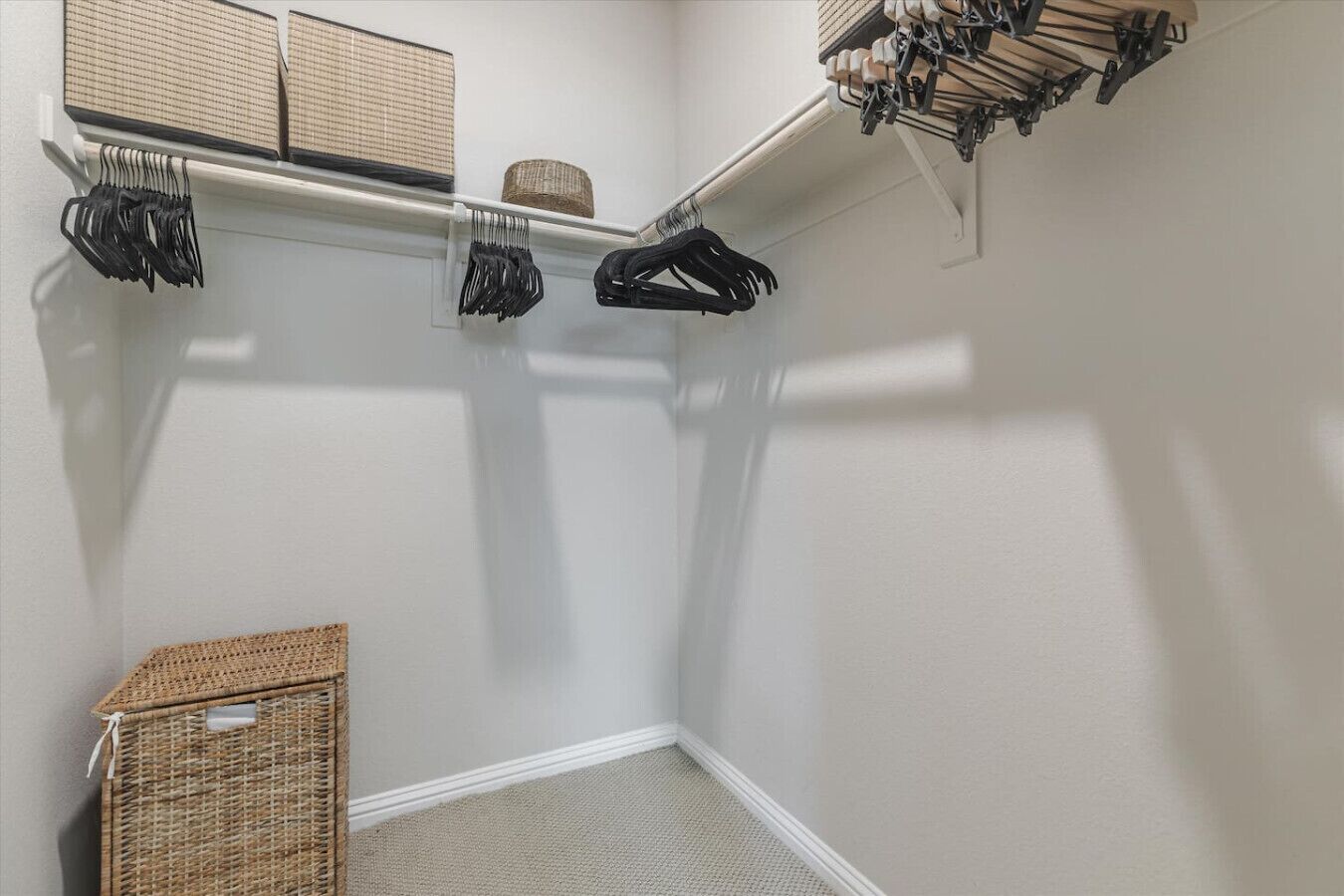 A corner closet with a hanging rod for clothes, a wicker basket, and a white wall.
