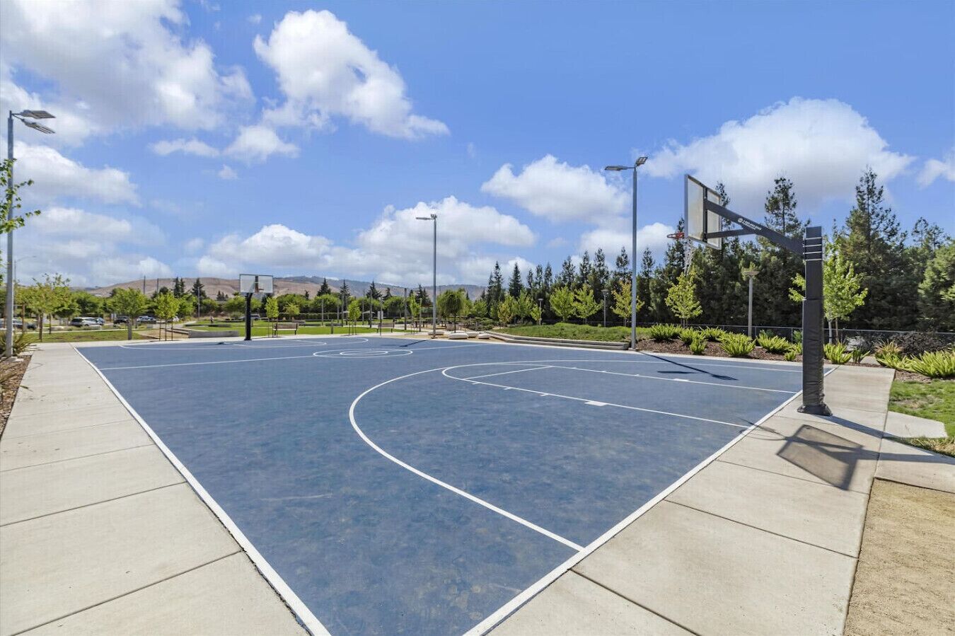 Ein Basketballplatz im Freien mit blauem Himmel, Bäumen und einer entfernten Bergkette.