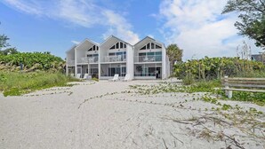 A beachfront property with a modern two-story building, a sandy beach in front, and a wooden fence. - Beachfront Paradise! Ground level with Heated pool (Holmes Beach)