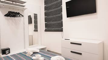 A modern hotel room with a bed, a bedside table, a wardrobe, a mirror, and a flat-screen TV mounted on the wall.