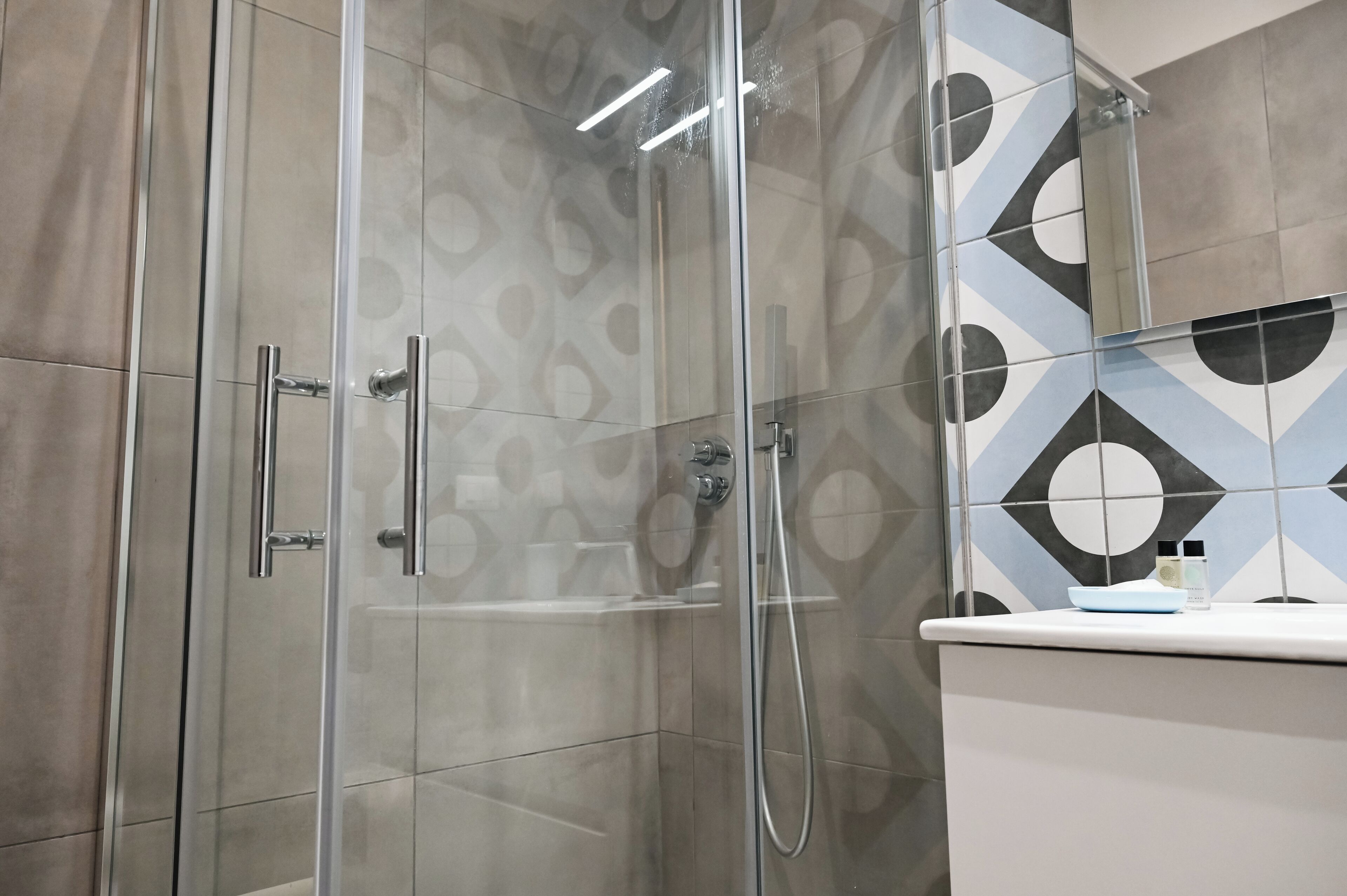 A modern bathroom with a glass-enclosed shower, a white sink, and patterned tiles.