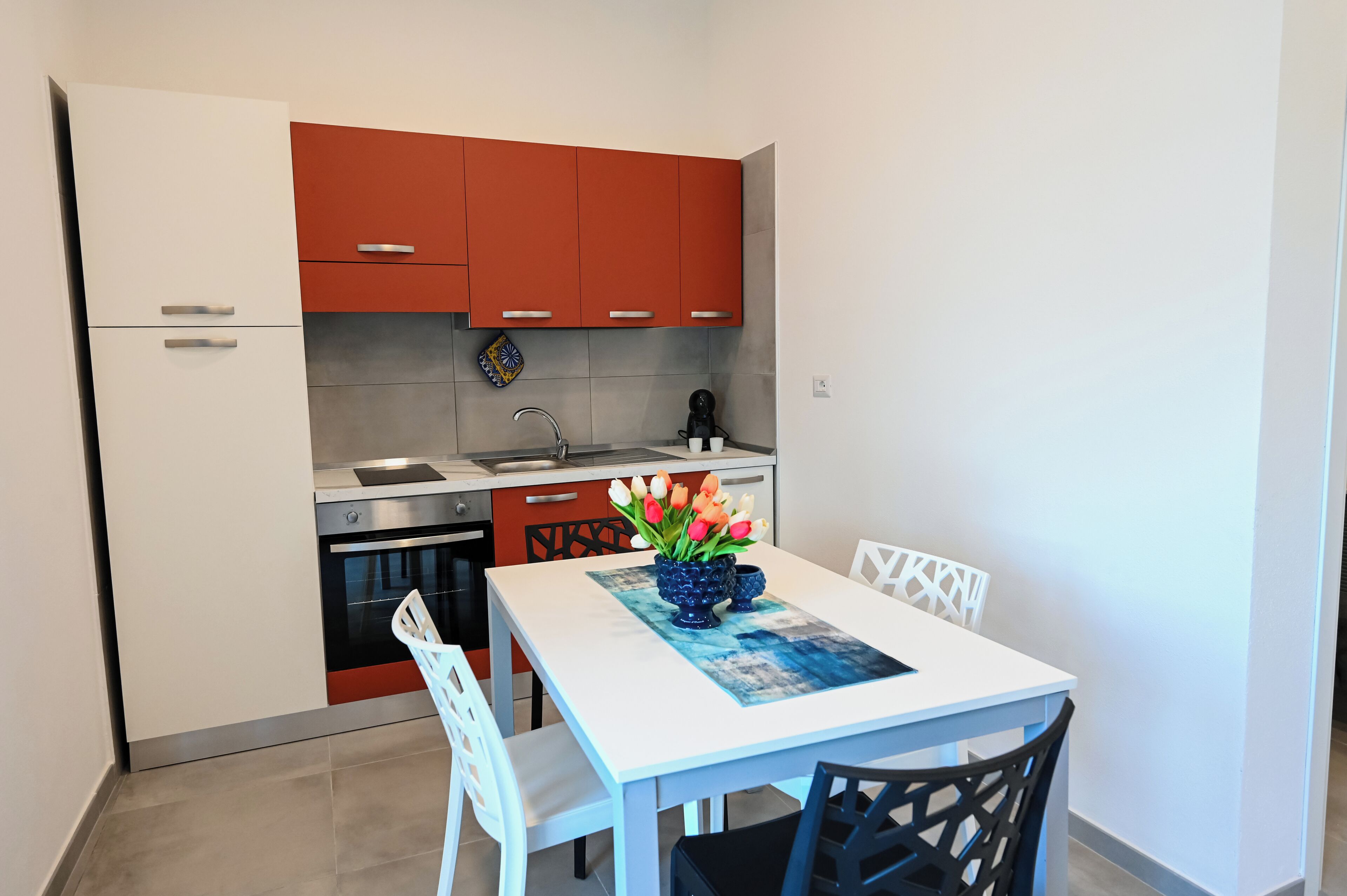 Une cuisine compacte avec des meubles blancs et rouges, un four en acier inoxydable et une table à manger avec des chaises.