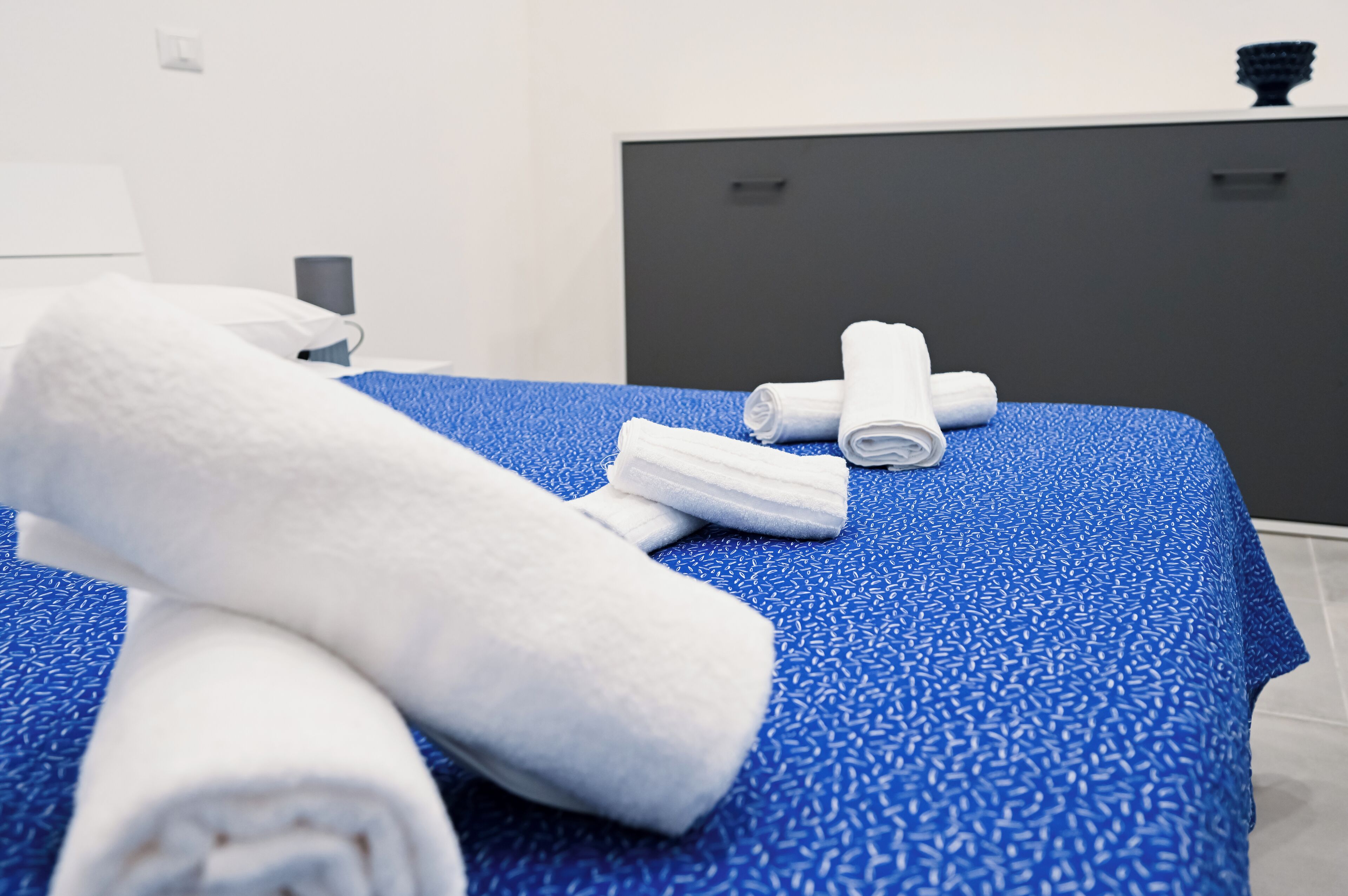A hotel room with a blue patterned bedspread, neatly folded white towels, and a dark-colored headboard.