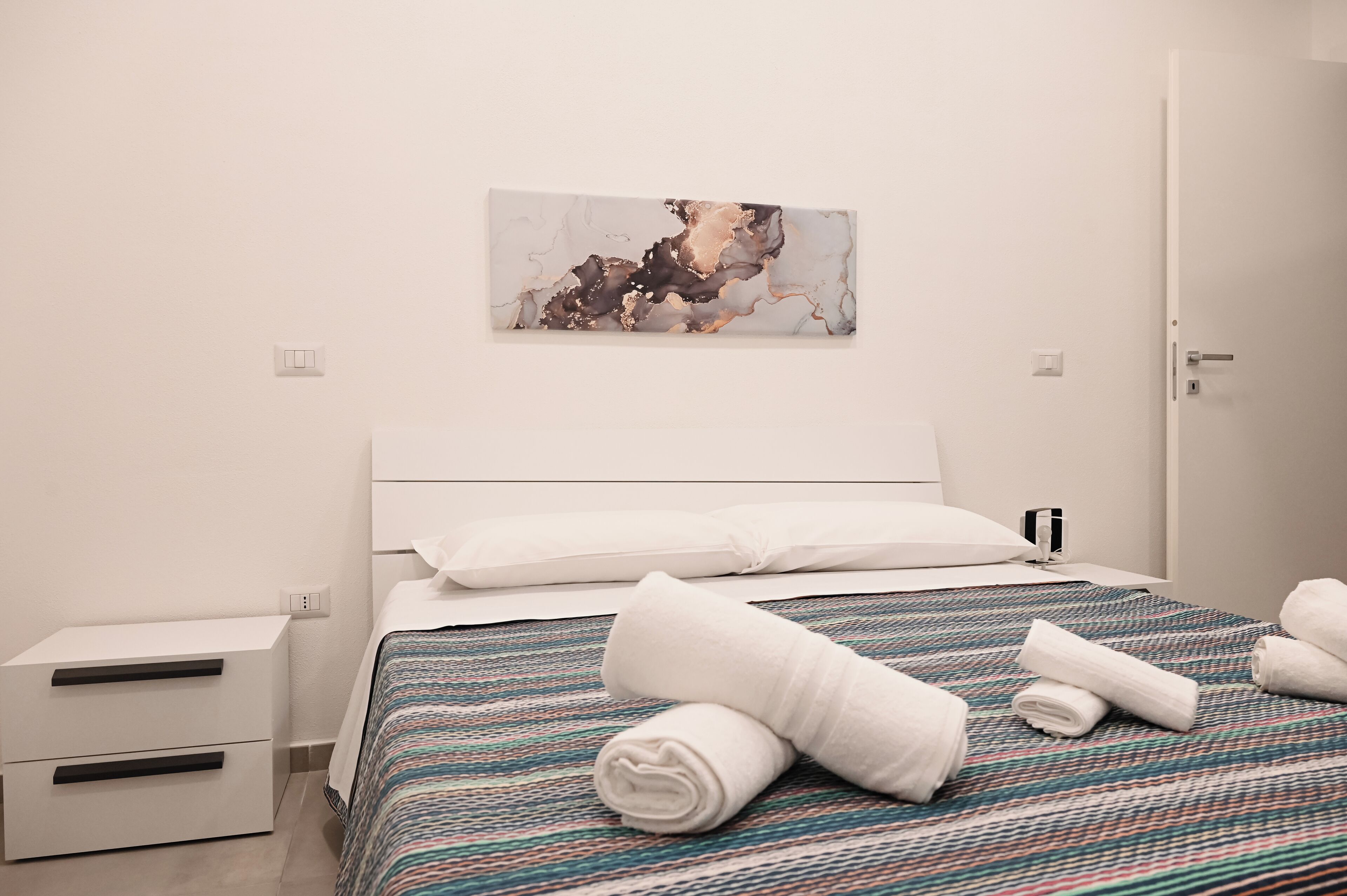 Ein ordentlich bezogenes Bett mit einer gestreiften Tagesdecke, einem weißen Kopfkissen und zusammengerollten Handtüchern daneben.