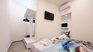 Une chambre d’hôtel comprenant un lit, un téléviseur fixé au mur, un miroir, un banc et une petite table avec des articles de toilette.