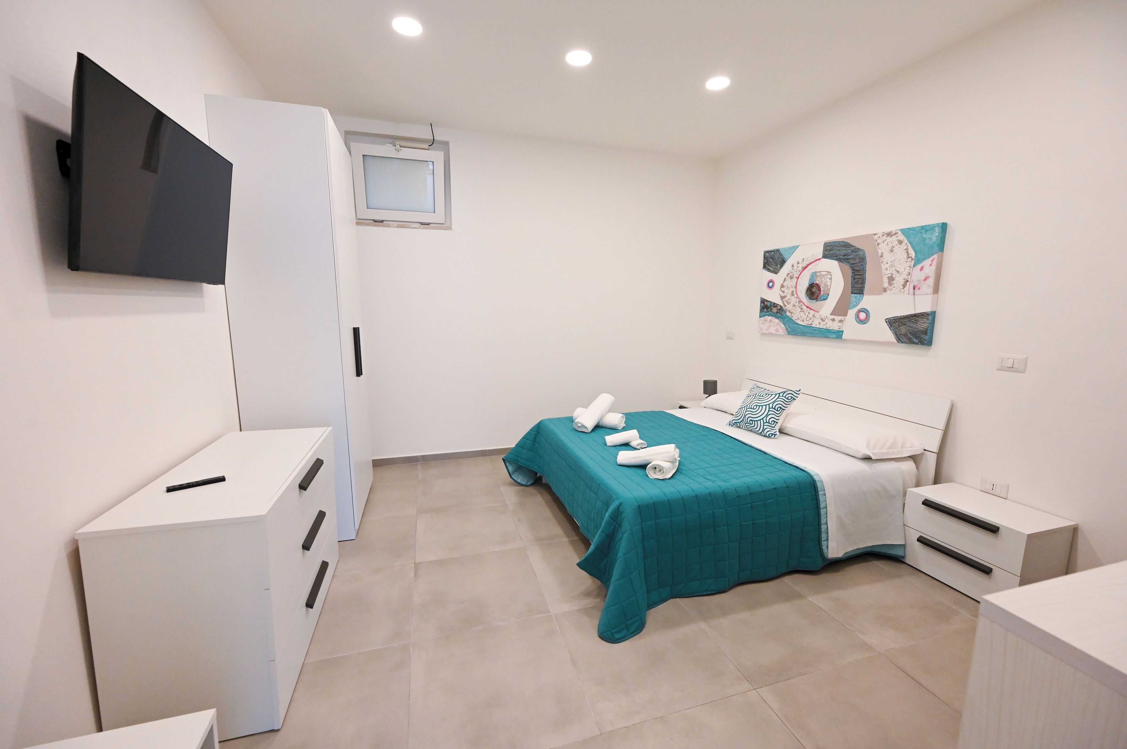 Un dormitorio con una cama, un televisor montado en la pared, una mesita de noche y un tocador.