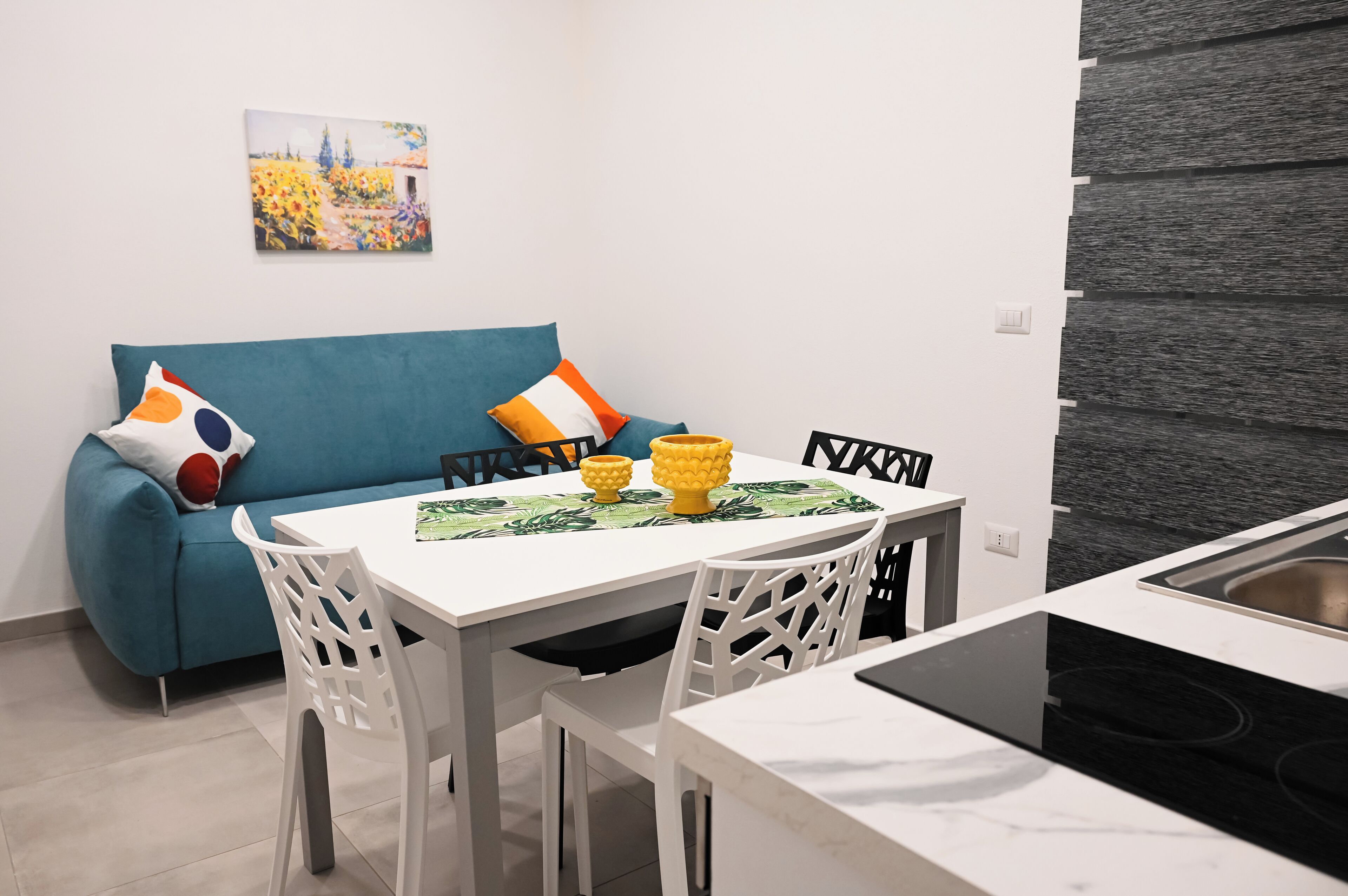 Una cucina moderna con un piano di lavoro bianco, un tavolo da pranzo con sedie bianche e un divano blu con cuscini colorati.