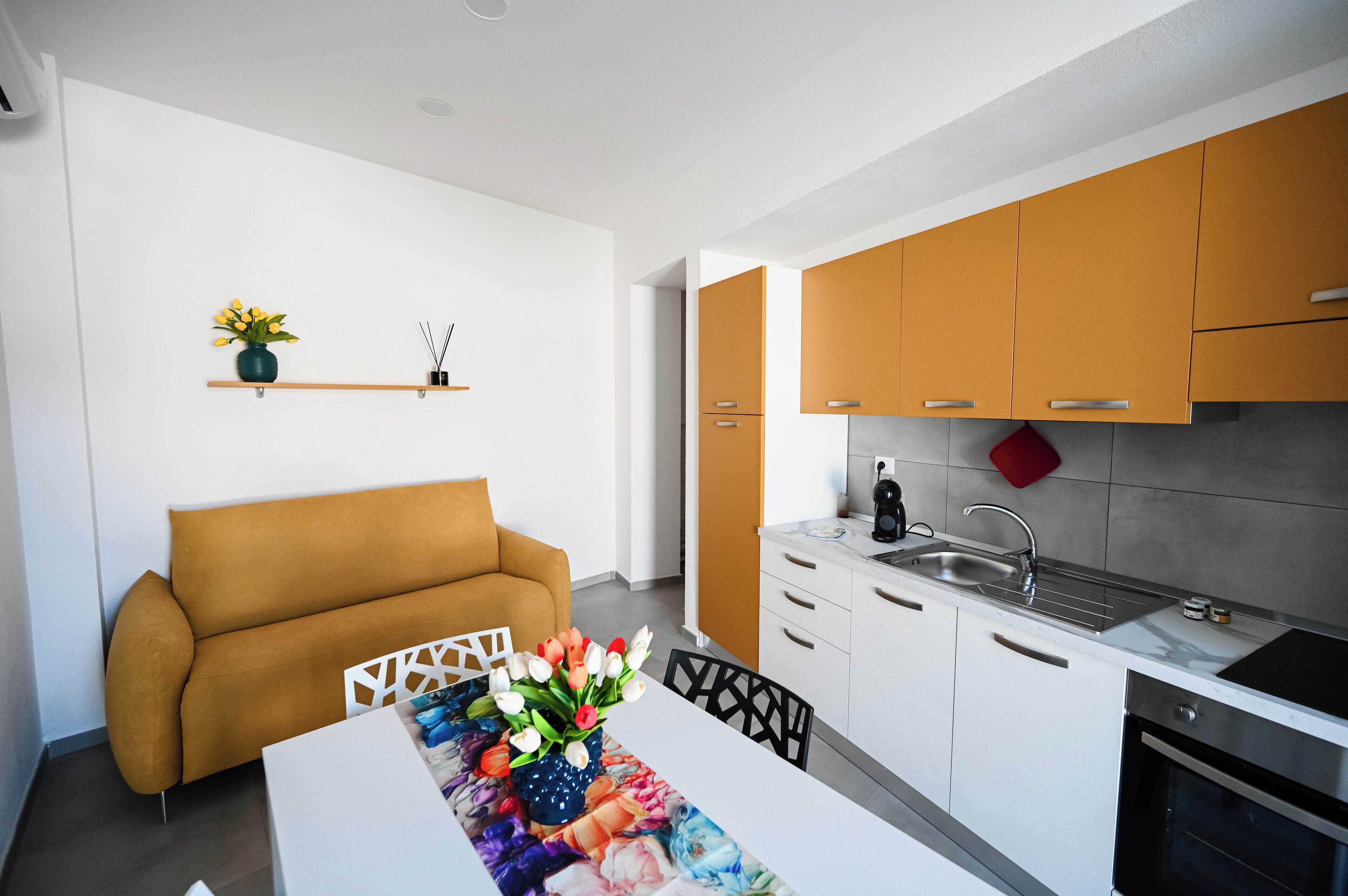 Una cocina moderna con armarios blancos y naranja, un lavamanos de acero inoxidable y una estufa negra.