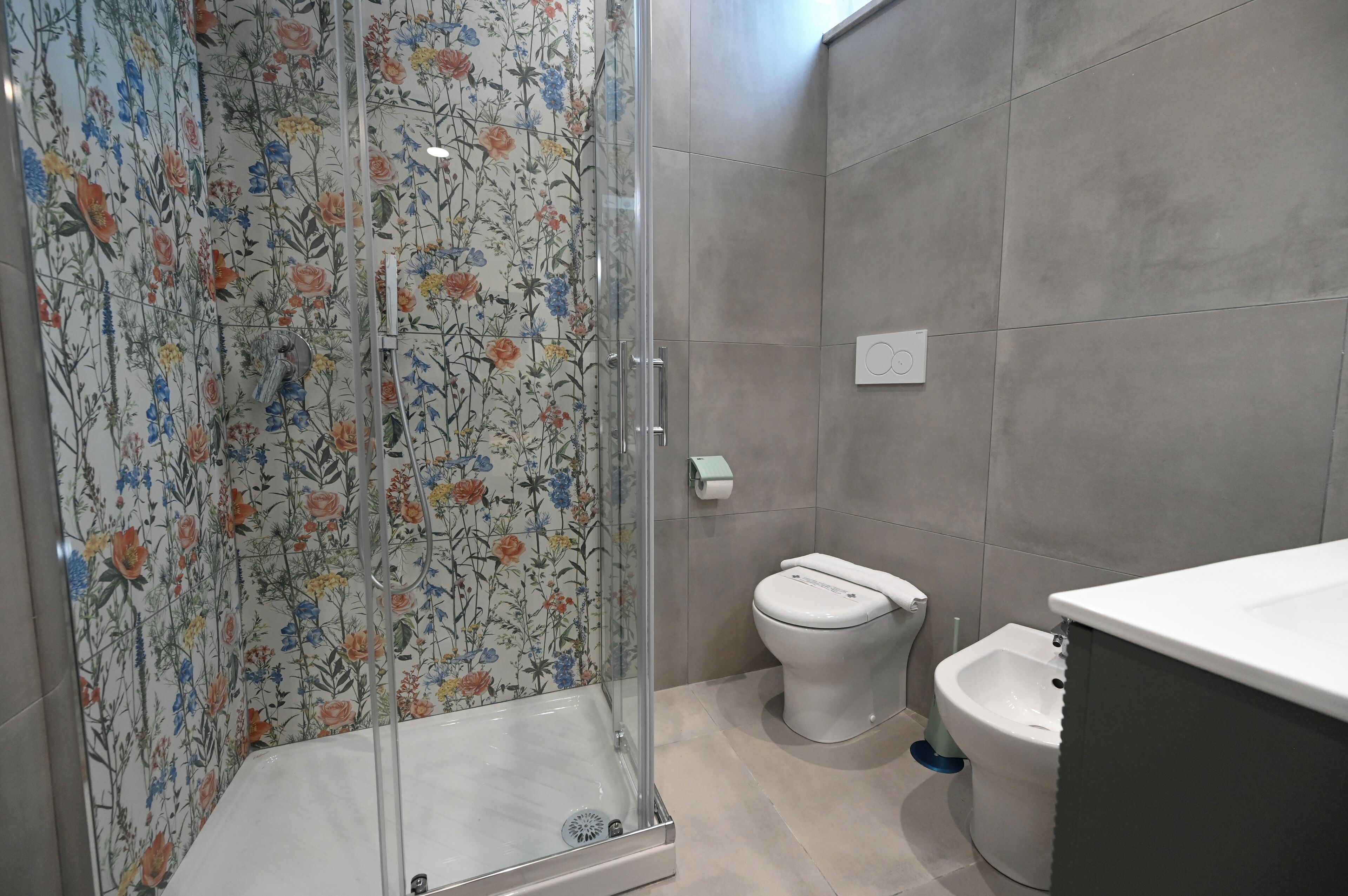 A bathroom with a shower, toilet, bidet, and tiled walls.