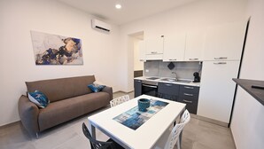 Une cuisine moderne avec des meubles blancs, une table à manger avec des chaises et un canapé agrémenté de coussins décoratifs.