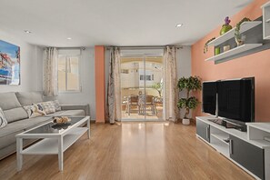 Un salon moderne comprenant un canapé, une table basse, un téléviseur et un balcon avec un coin repas.