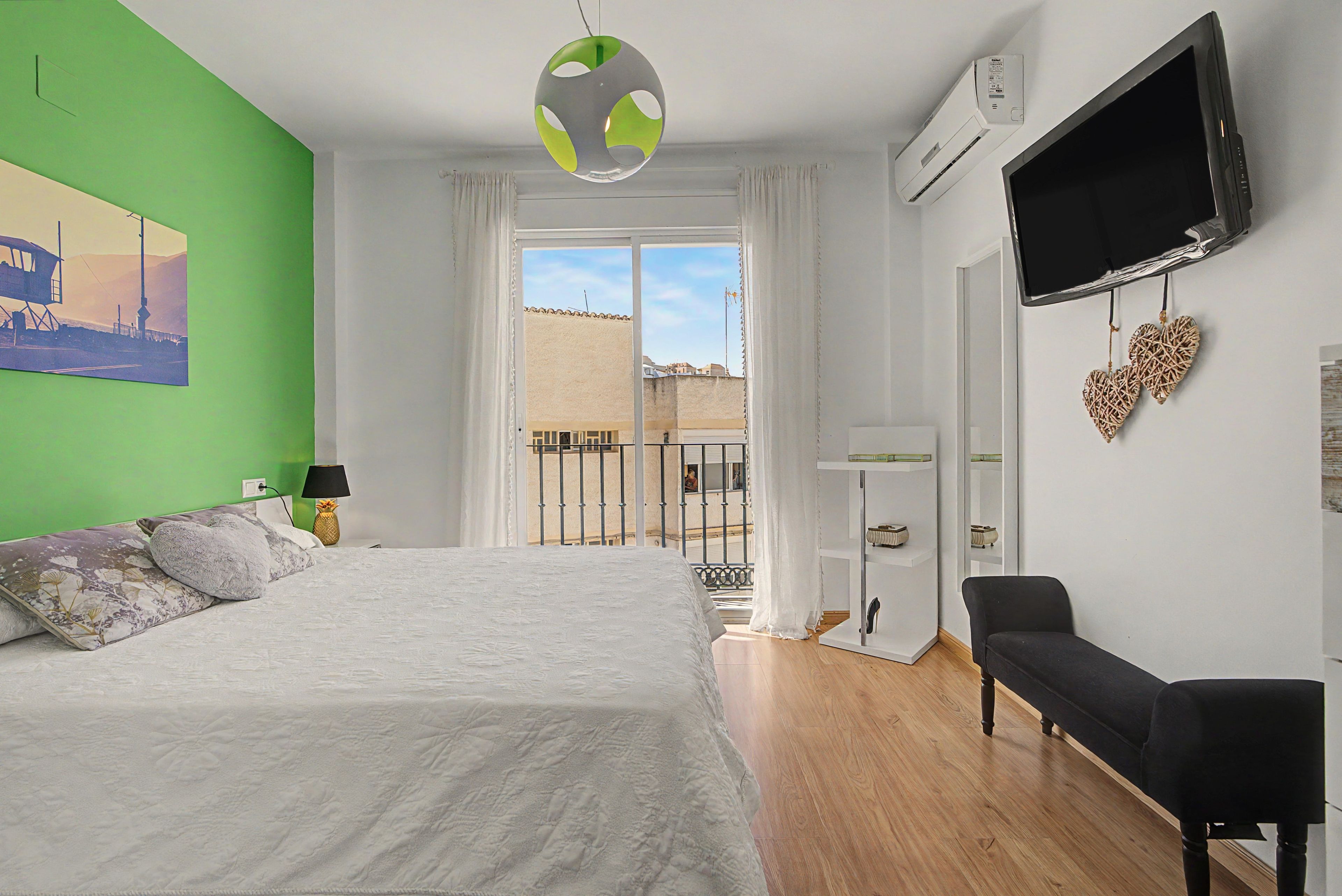 Un dormitorio con cama, televisor, aire acondicionado y vistas al exterior.