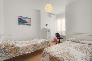 Een slaapkamer met twee bedden, een bureau, een stoel, een garderobe en een schilderij aan de muur.