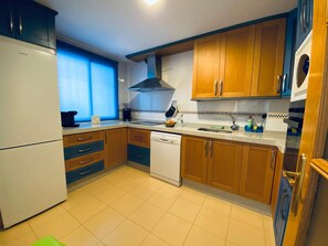 A kitchen with wooden cabinets, a dishwasher, a stove, and a window with blue curtains.