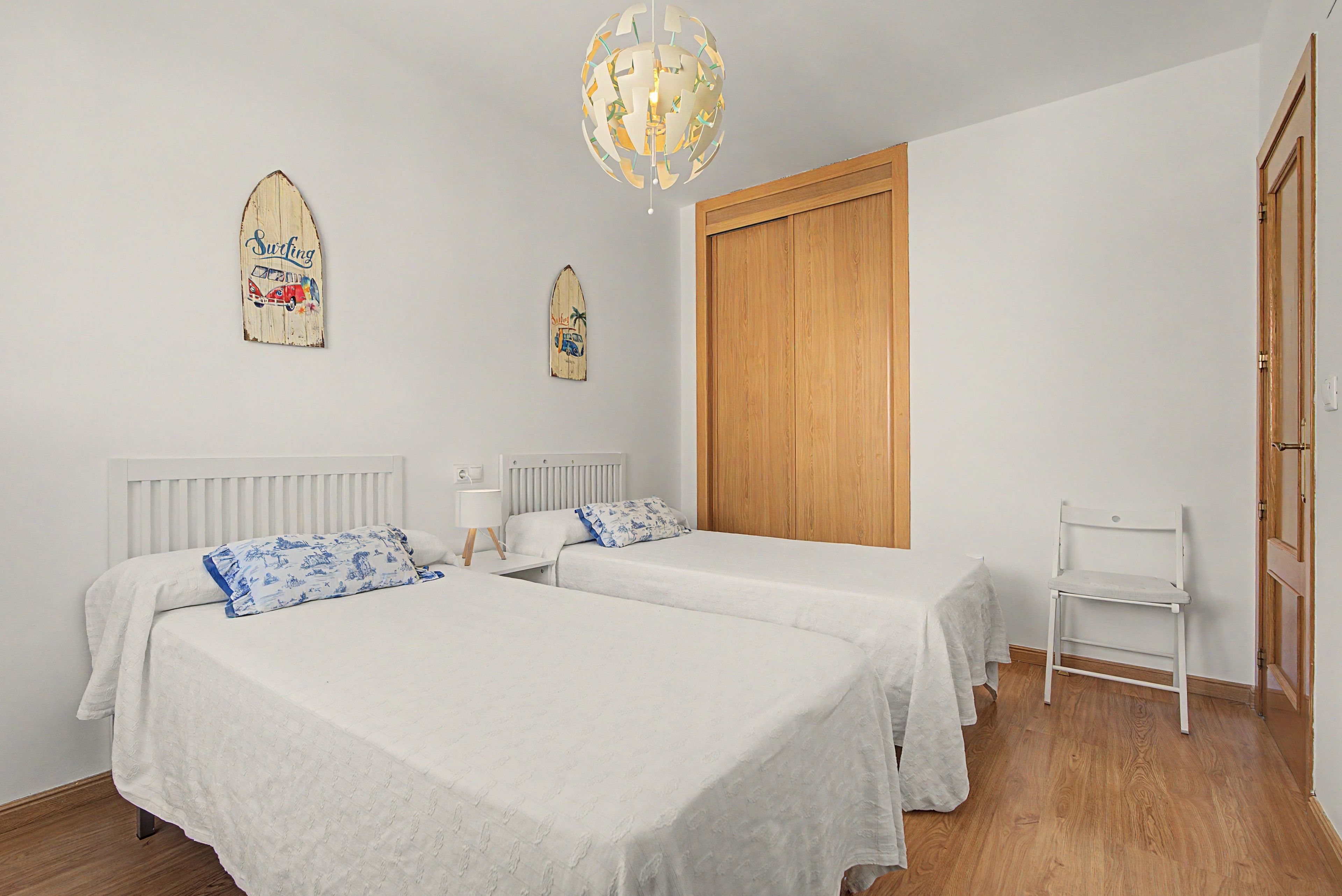 Un dormitorio con dos camas, un armario de madera, una silla y un adorno en la pared.