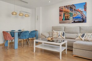 A modern living room with a dining area, a sofa, and a painting of a street scene.