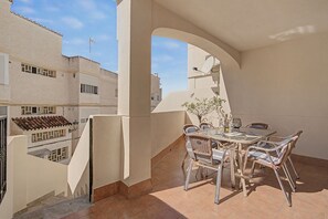 Een balkon met een tafel en stoelen, een bloempot en uitzicht op omliggende gebouwen.