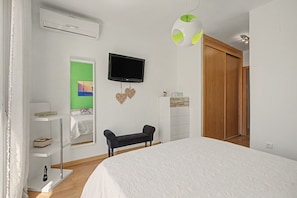 Een slaapkamer met een bed, een televisie, een kledingkast en een bankje.