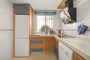 A kitchen with a refrigerator, wooden cabinets, a window, and a countertop with various items.