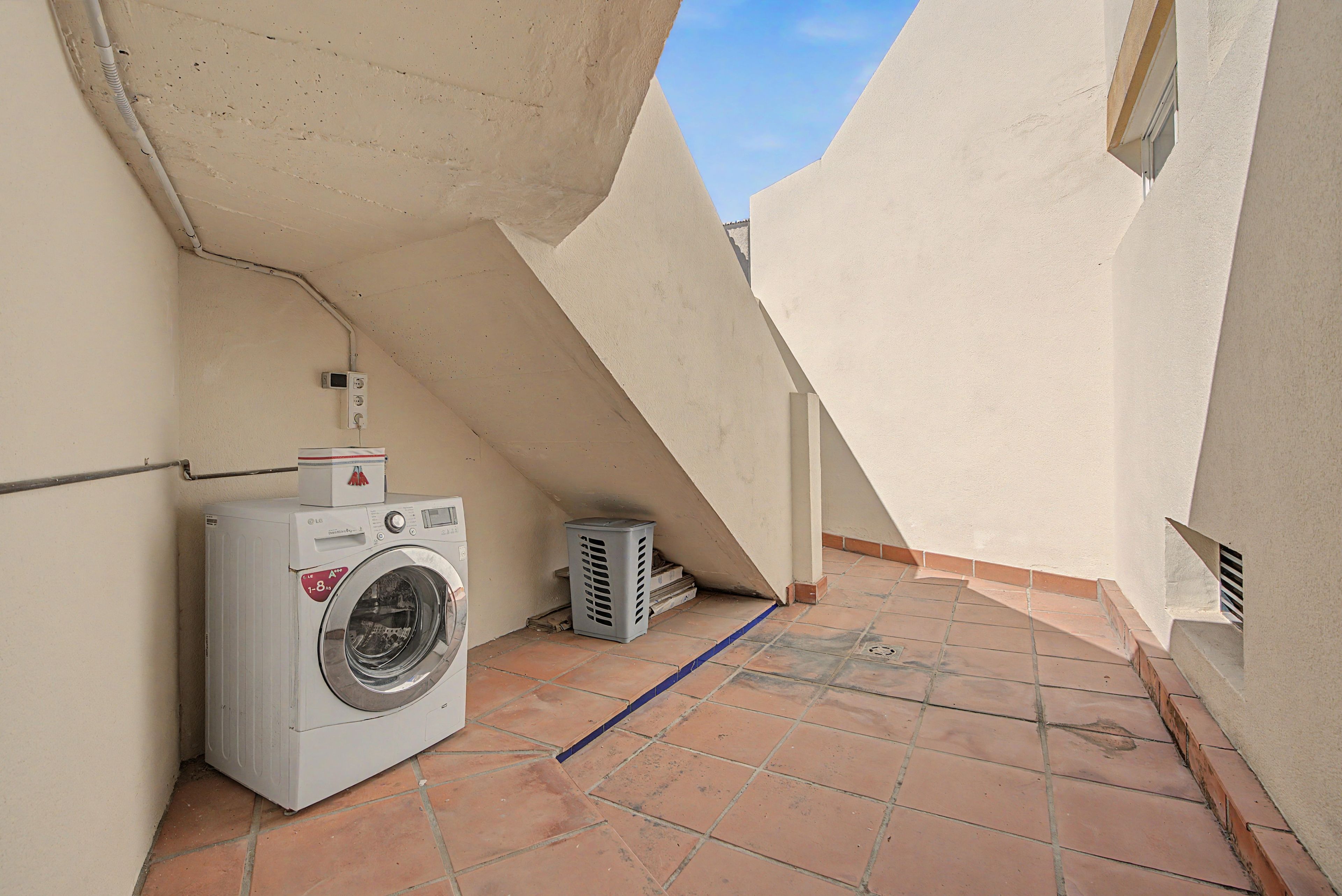 Un'area lavanderia con lavatrice, termosifone e cestino su pavimento piastrellato.