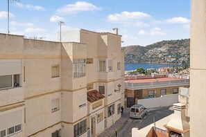 Una calle estrecha entre edificios, con vista a una ladera y un cuerpo de agua.