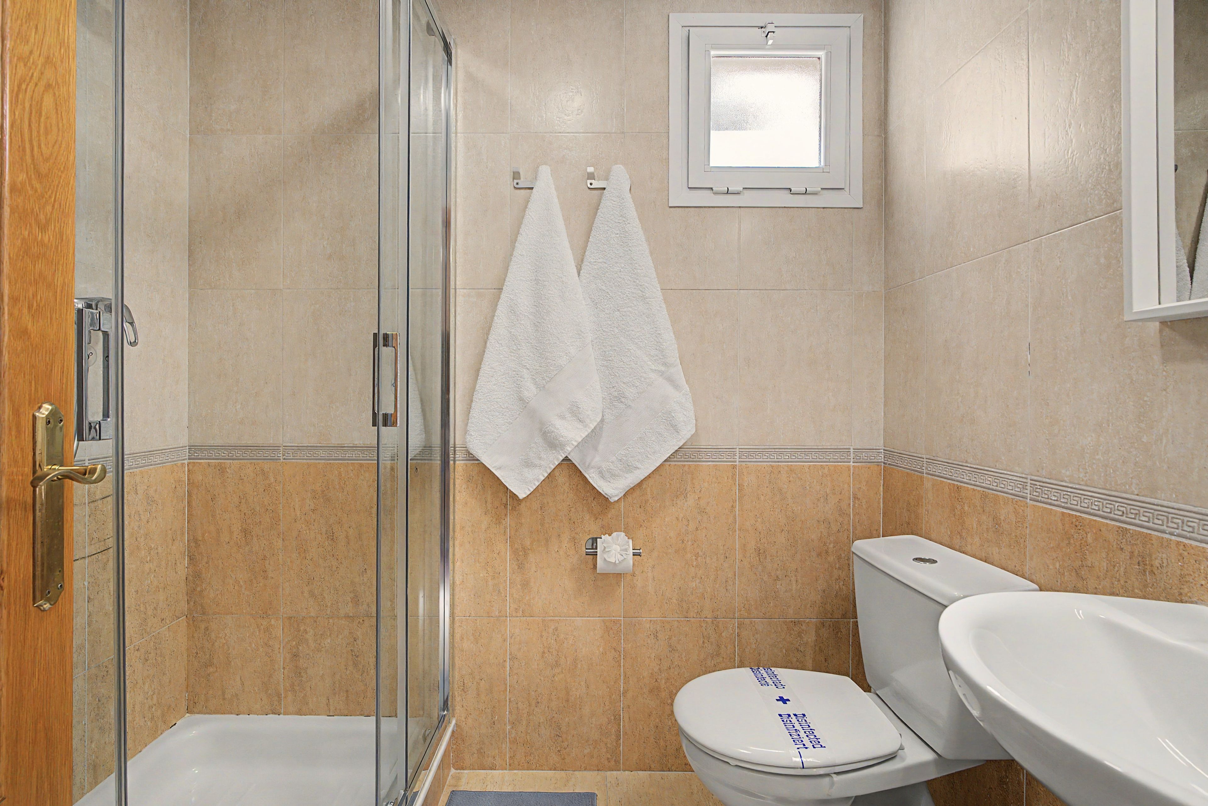 Et badeværelse med glasvæg omkring bruseren, toilet og håndvask.
