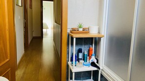 Un couloir avec une porte en bois, une petite étagère contenant des articles de toilette et une vue sur une autre pièce.