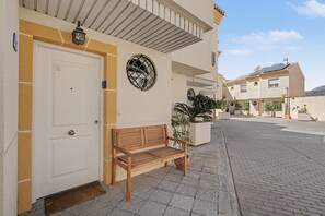 Un edificio con una puerta blanca, un banco de madera y plantas en macetas.