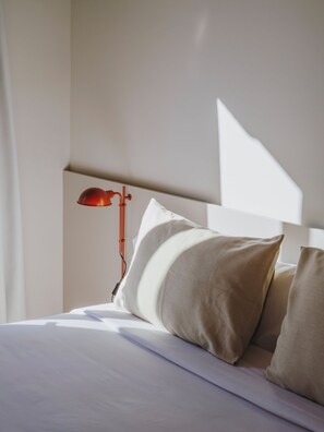 A neatly made bed with pillows, a red lamp, and a white headboard in a hotel room.