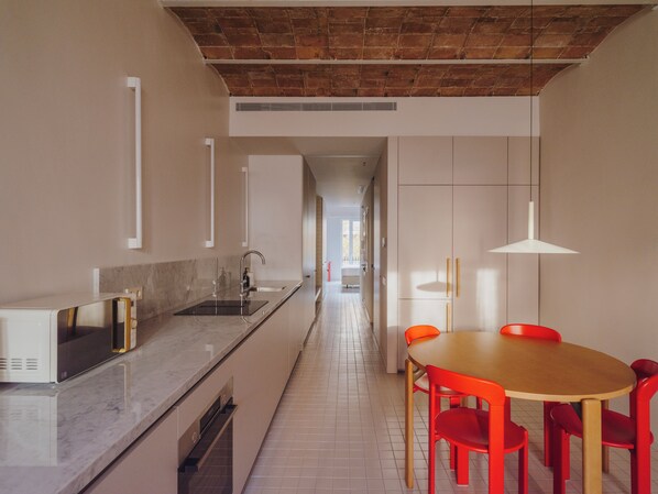 Une cuisine moderne dotée d’un plan de travail en marbre, d’un four encastré et d’un coin repas avec une table en bois et des chaises rouges.
