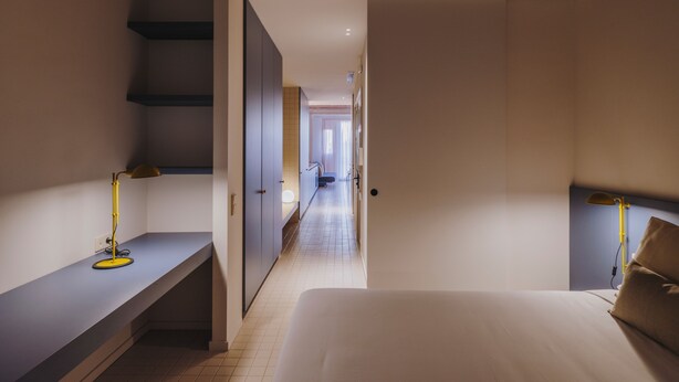 Una habitación de hotel con cama, escritorio, silla, armario y escalera.