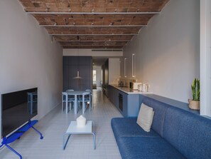 A modern living room with a sofa, TV, and a dining area with chairs and a table.