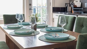 Une table à manger dressée avec des assiettes, des couverts et des verres à vin, avec la cuisine en arrière-plan.