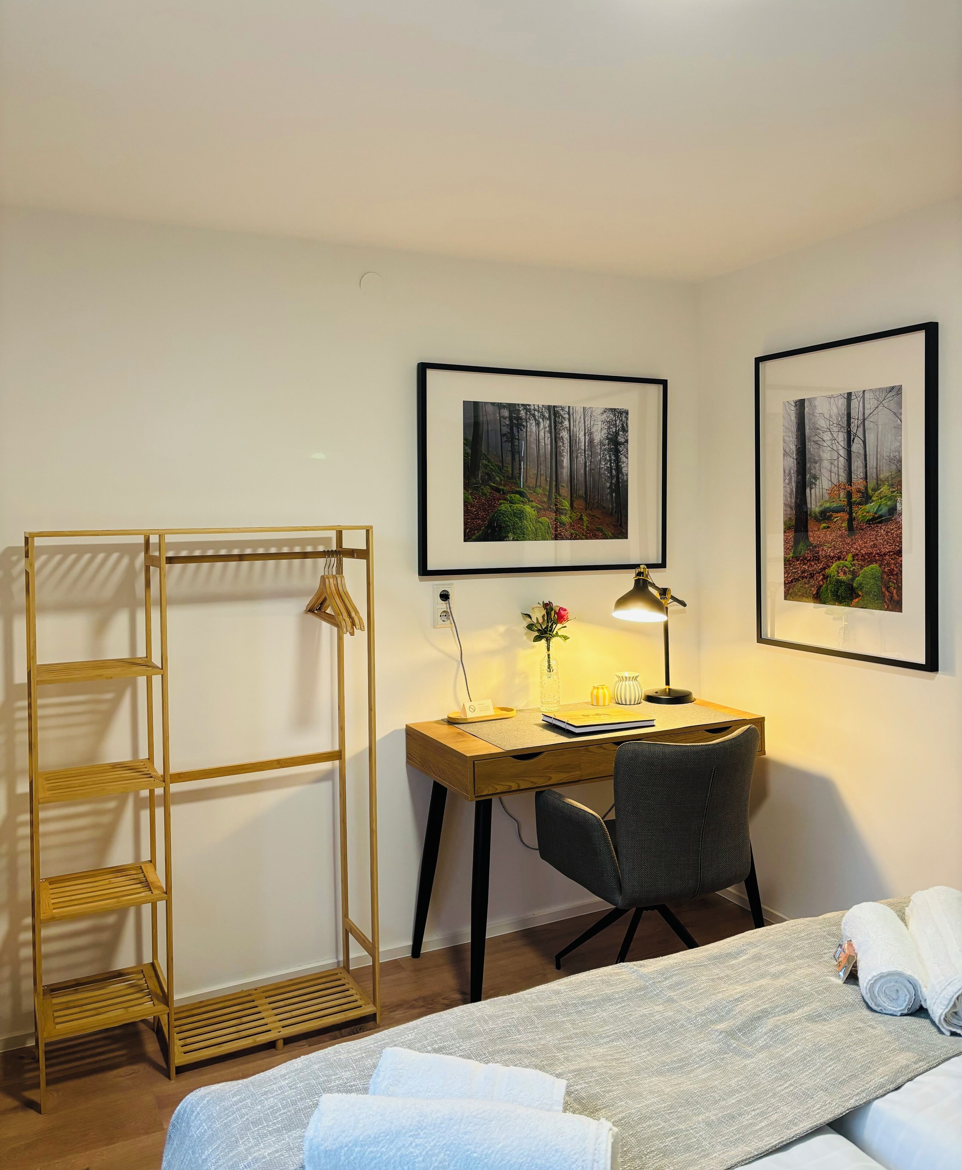 Een hotelkamer met een bed, een bureau met stoel, een houten wandplank en twee ingelijste foto's aan de muur.