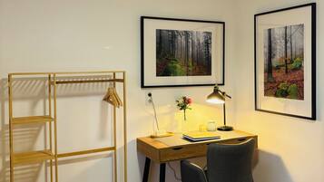 Een hotelkamer met een bed, een bureau met stoel, een houten wandplank en twee ingelijste foto's aan de muur.