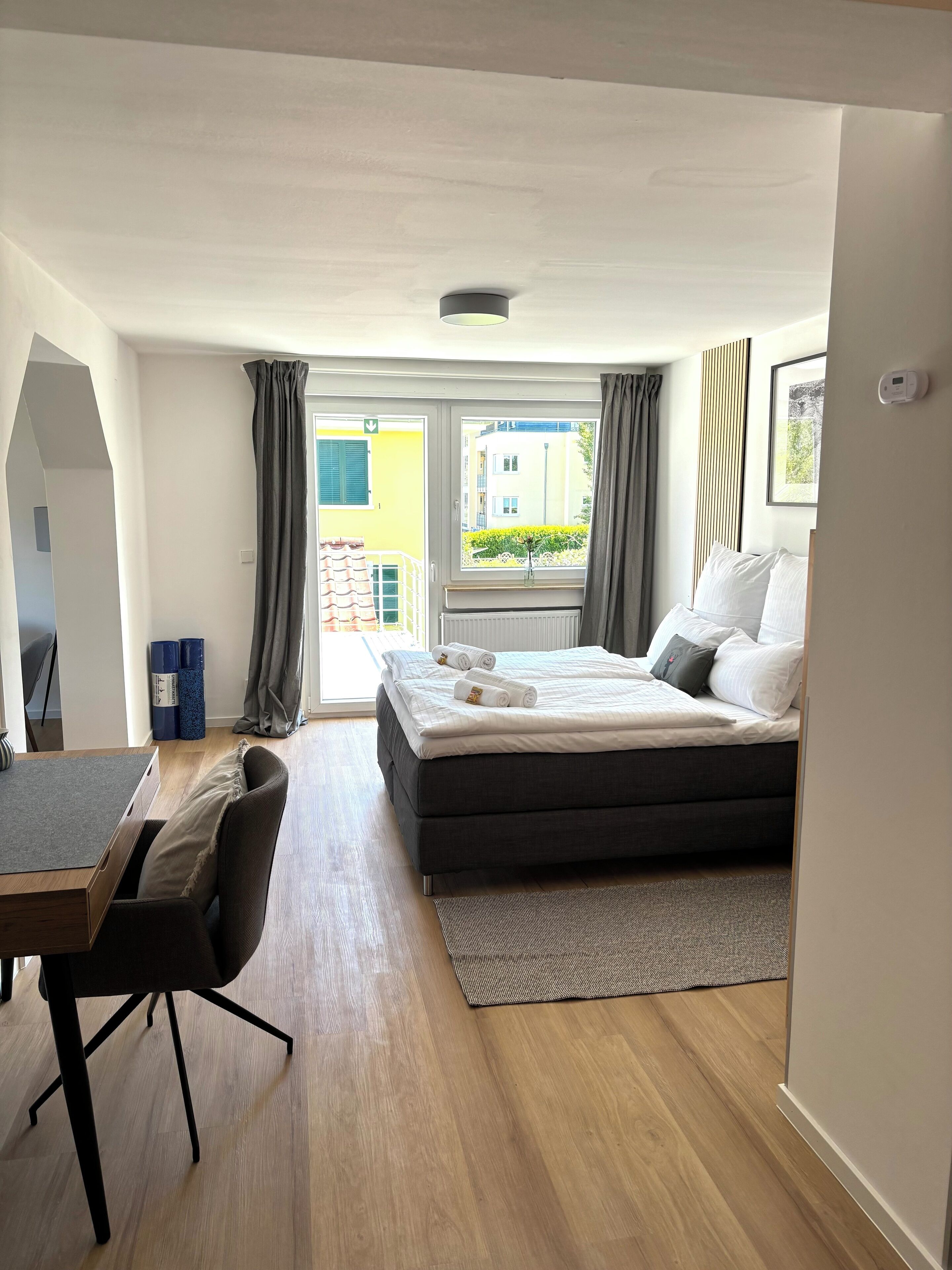 A modern hotel room with a bed, a desk, and a view of the outside.