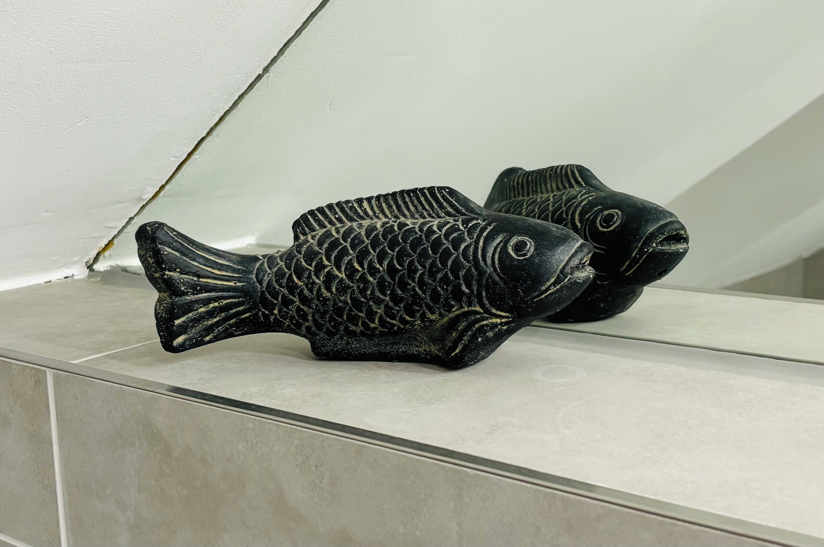 A pair of black fish-shaped sculptures on a tiled ledge.